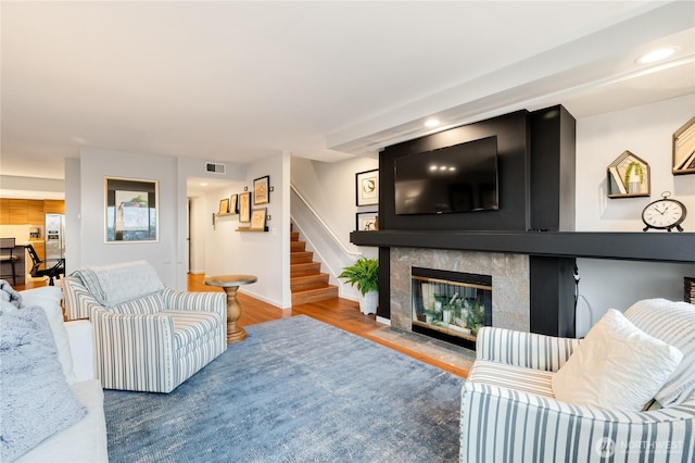 living area with stairway, wood finished floors, baseboards, visible vents, and a tile fireplace