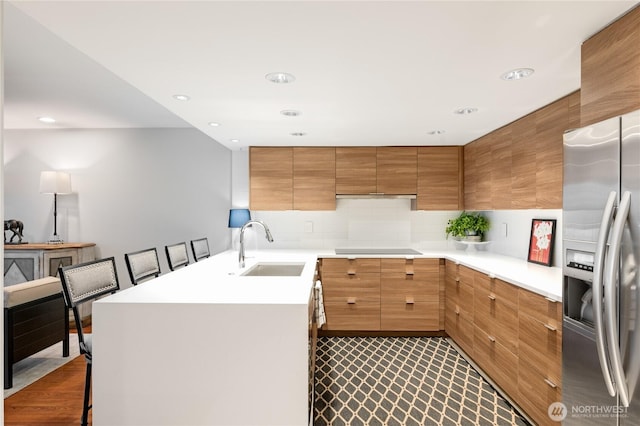 kitchen with stainless steel refrigerator with ice dispenser, a sink, light countertops, decorative backsplash, and black electric stovetop