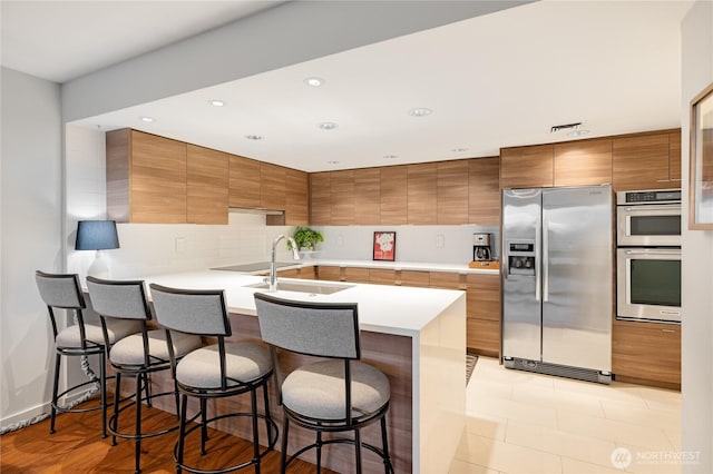 kitchen with brown cabinetry, a peninsula, light countertops, appliances with stainless steel finishes, and a kitchen bar