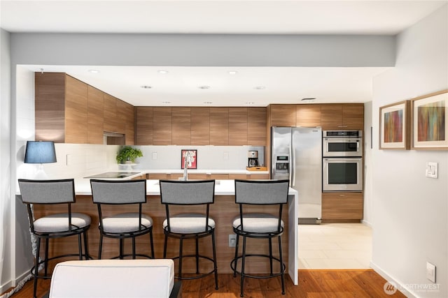 kitchen with a breakfast bar area, brown cabinets, appliances with stainless steel finishes, a peninsula, and modern cabinets