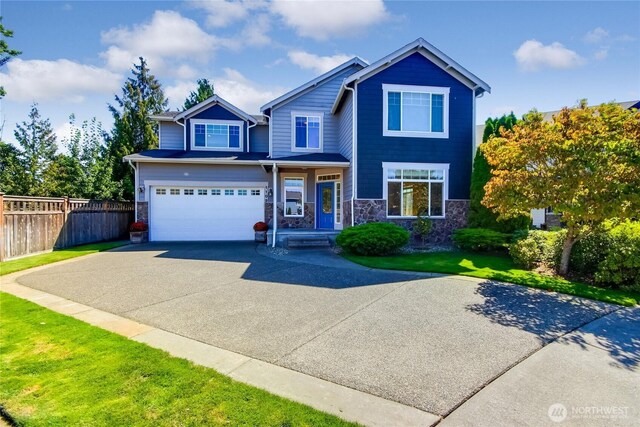 view of front of property featuring a front lawn, driveway, stone siding, fence, and an attached garage