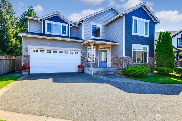 craftsman house featuring an attached garage, fence, stone siding, and driveway