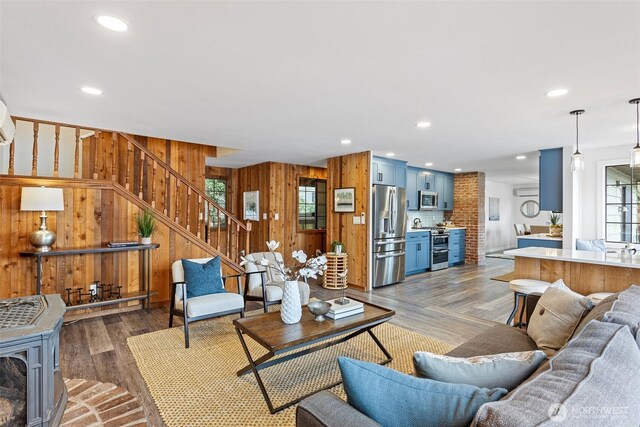 living room with wooden walls, wood finished floors, recessed lighting, stairway, and a wood stove