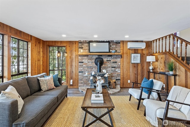 living room featuring light wood-style flooring, wood walls, stairway, a wood stove, and an AC wall unit