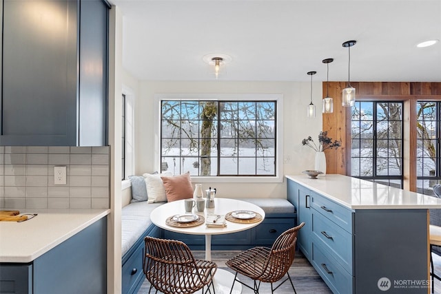 kitchen with blue cabinetry, light countertops, tasteful backsplash, decorative light fixtures, and a peninsula