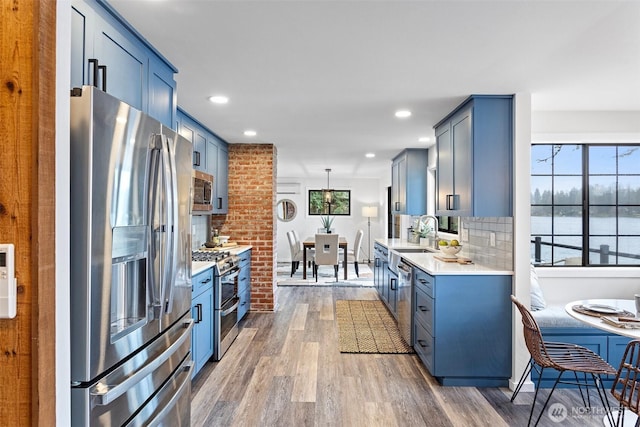 kitchen featuring light countertops, a sink, backsplash, wood finished floors, and stainless steel appliances