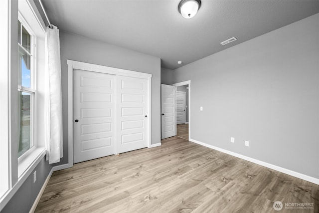 unfurnished bedroom featuring wood finished floors, visible vents, a closet, and baseboards