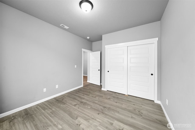 unfurnished bedroom with a closet, visible vents, baseboards, and wood finished floors