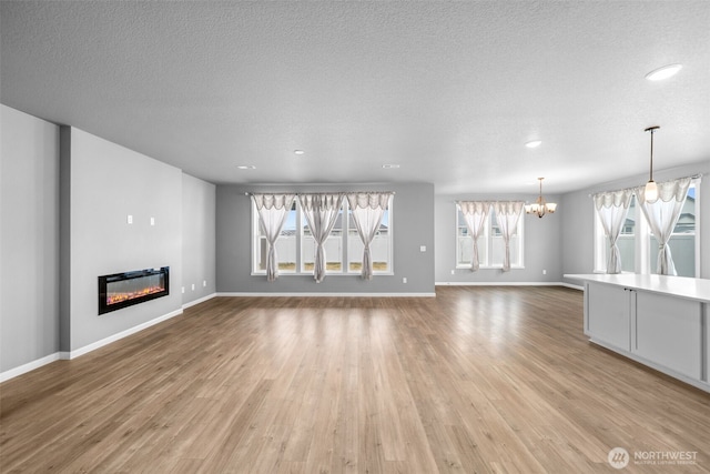 unfurnished living room with a textured ceiling, a glass covered fireplace, an inviting chandelier, light wood finished floors, and baseboards