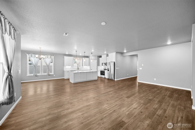unfurnished living room featuring a notable chandelier, a textured ceiling, baseboards, and dark wood-style flooring