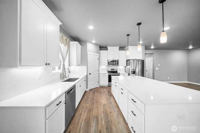 kitchen with hardwood / wood-style floors, a kitchen island, a sink, light countertops, and appliances with stainless steel finishes