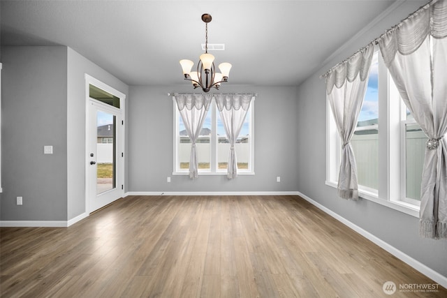 unfurnished dining area featuring a wealth of natural light, baseboards, a notable chandelier, and wood finished floors