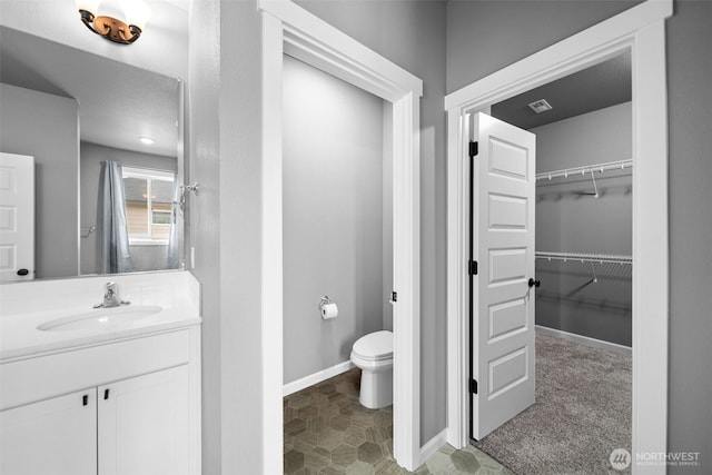 bathroom featuring vanity, a spacious closet, toilet, and baseboards