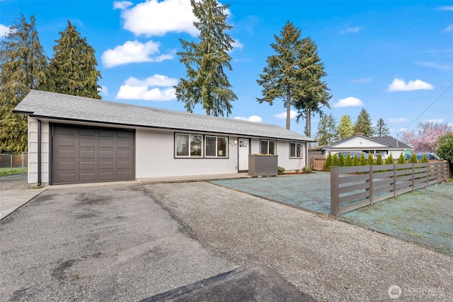 ranch-style house featuring driveway, a garage, fence, and a shingled roof