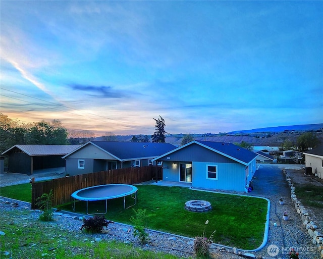 back of house featuring a lawn, a trampoline, a fire pit, and fence private yard