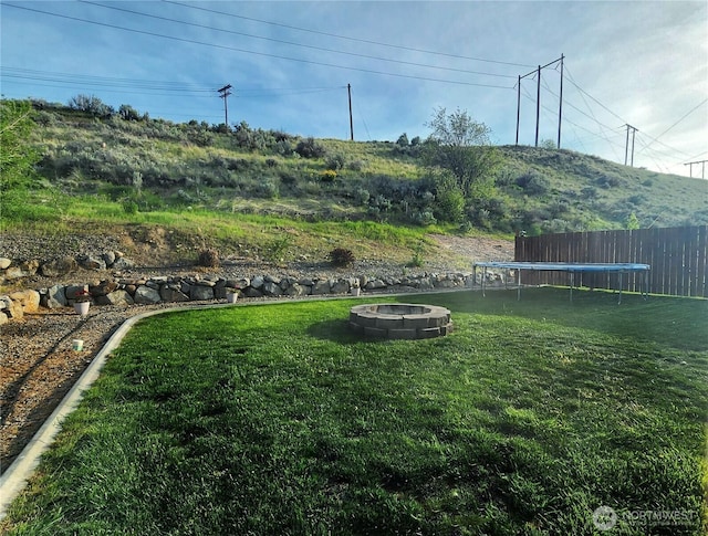view of yard with fence, an outdoor fire pit, and a trampoline