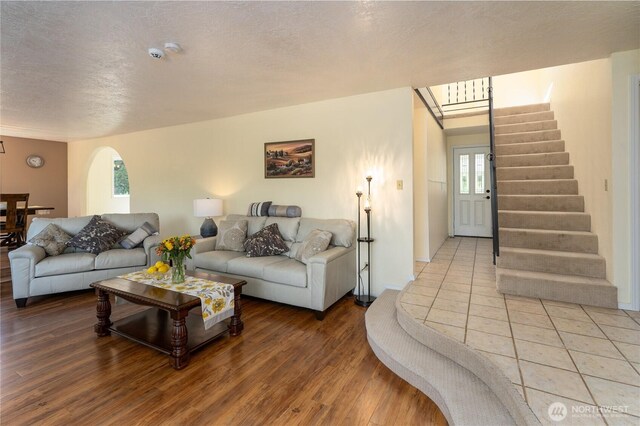 living room with a textured ceiling, stairs, light wood-style flooring, and arched walkways