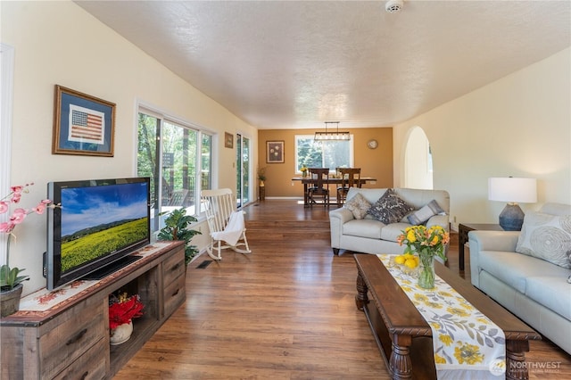 living area with arched walkways, wood finished floors, and a chandelier