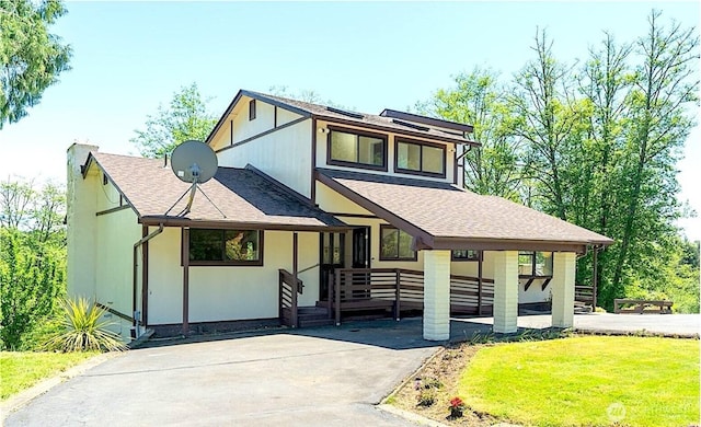 view of front facade with a porch, driveway, a chimney, a front yard, and a shingled roof