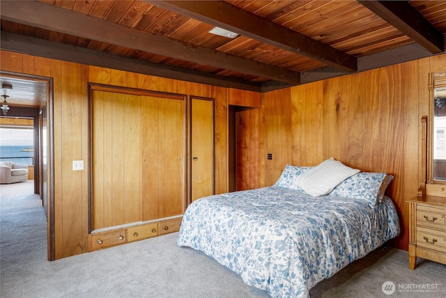 bedroom with beamed ceiling, a closet, wood ceiling, carpet flooring, and wooden walls