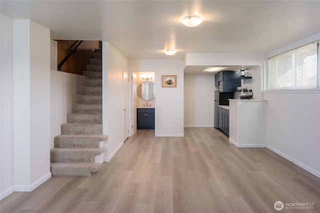 interior space featuring a sink, baseboards, light wood finished floors, and stairs
