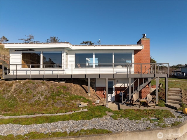 rear view of property featuring a wooden deck, stairway, a patio area, brick siding, and a chimney