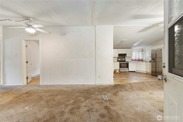 unfurnished living room with a textured ceiling, visible vents, a ceiling fan, vaulted ceiling, and light colored carpet