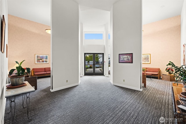 hall featuring a high ceiling, baseboards, and dark carpet