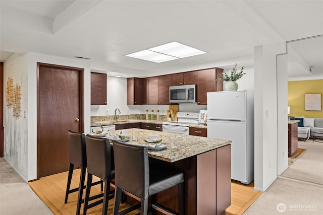 kitchen with white appliances, a breakfast bar area, a sink, light carpet, and a center island