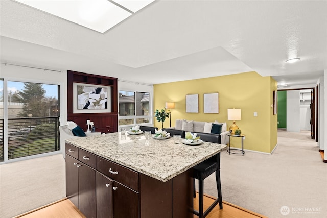 kitchen featuring light carpet, dark brown cabinets, a breakfast bar, and light stone countertops