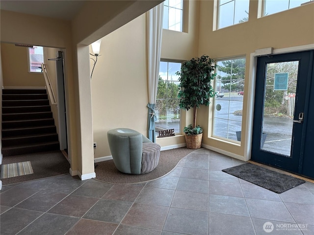 tiled entryway with stairs, a high ceiling, and baseboards