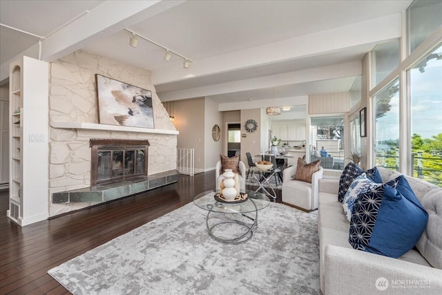 living room featuring rail lighting, a stone fireplace, baseboards, and hardwood / wood-style floors