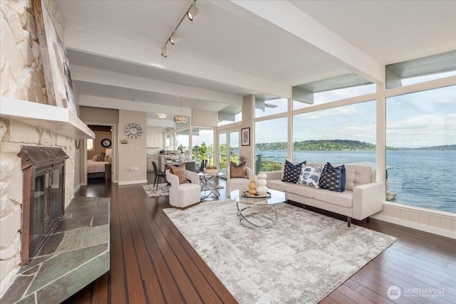 living room with track lighting, baseboards, beamed ceiling, dark wood-style floors, and a water view