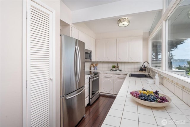 kitchen with a sink, stainless steel appliances, white cabinets, and tile countertops