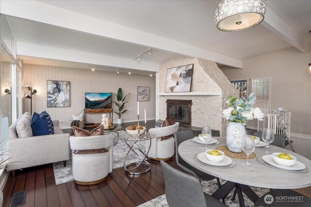 dining space with a stone fireplace, visible vents, track lighting, beamed ceiling, and wood-type flooring