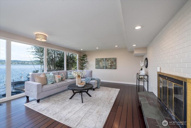 living room with recessed lighting, dark wood-style flooring, a water view, and a fireplace