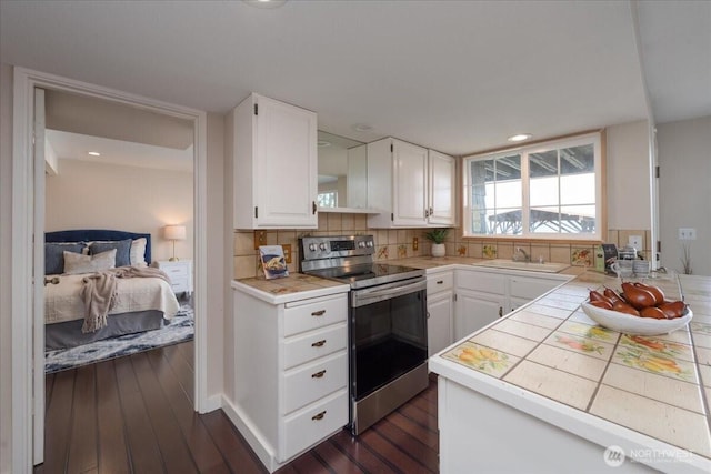 kitchen featuring decorative backsplash, electric range, tile countertops, white cabinets, and a sink