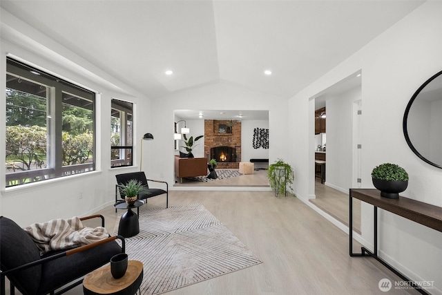 living area with vaulted ceiling, recessed lighting, light wood-type flooring, baseboards, and a brick fireplace