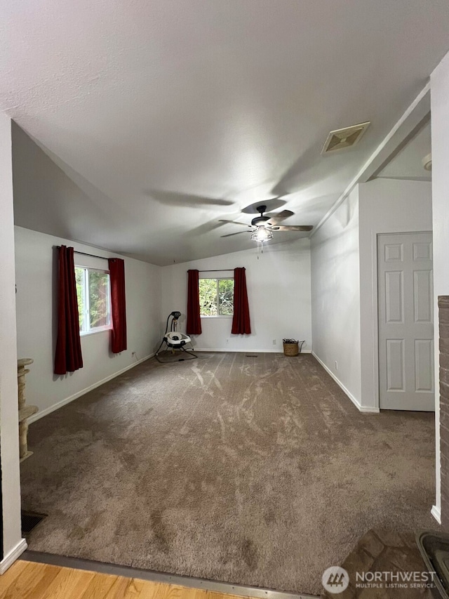 unfurnished living room with plenty of natural light, carpet, visible vents, and ceiling fan