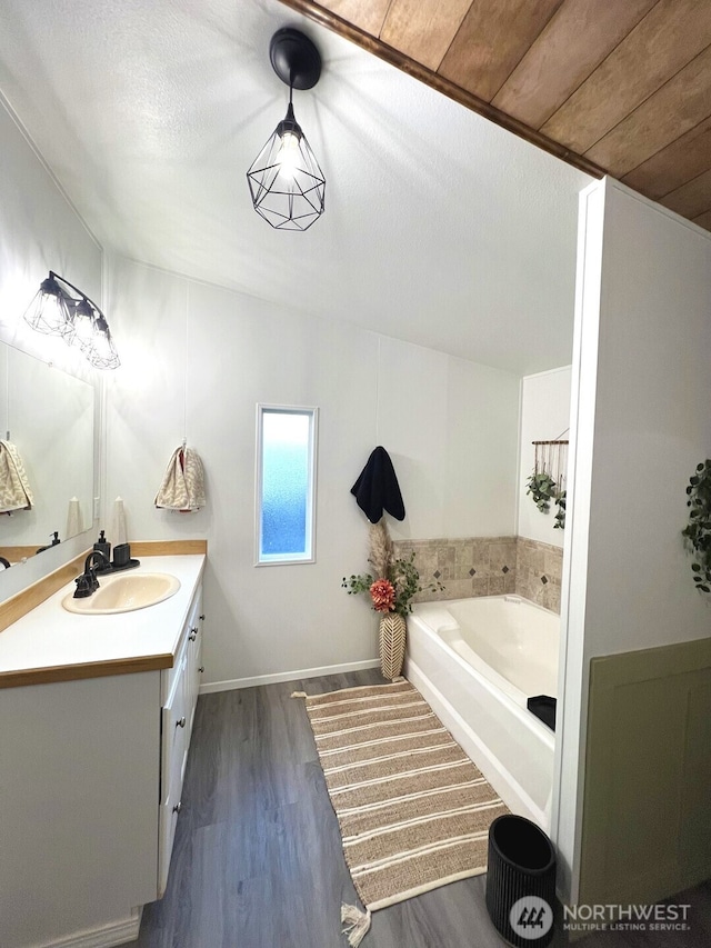 full bathroom featuring vanity, wood finished floors, baseboards, a textured ceiling, and a bath