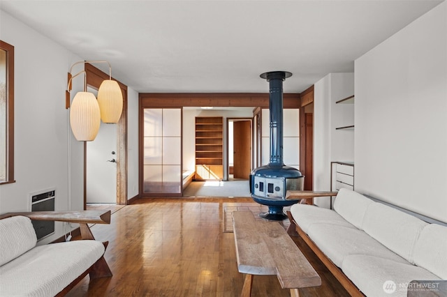 living area with heating unit, wood finished floors, and a wood stove