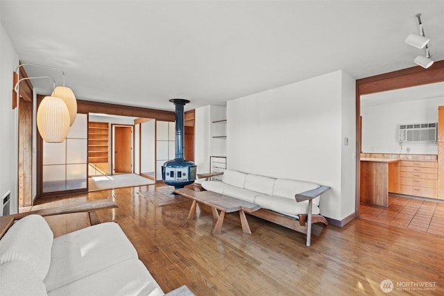 living room with a wall mounted air conditioner, rail lighting, wood finished floors, built in shelves, and a wood stove