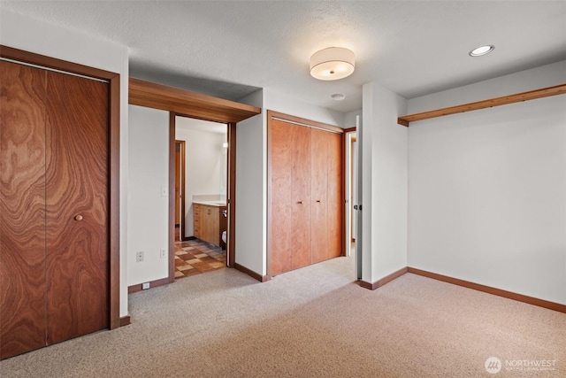 unfurnished bedroom with light carpet, baseboards, two closets, and connected bathroom