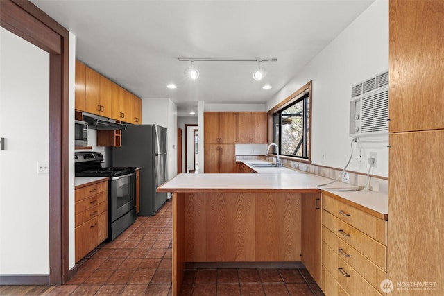 kitchen with light countertops, a peninsula, stainless steel appliances, under cabinet range hood, and a sink