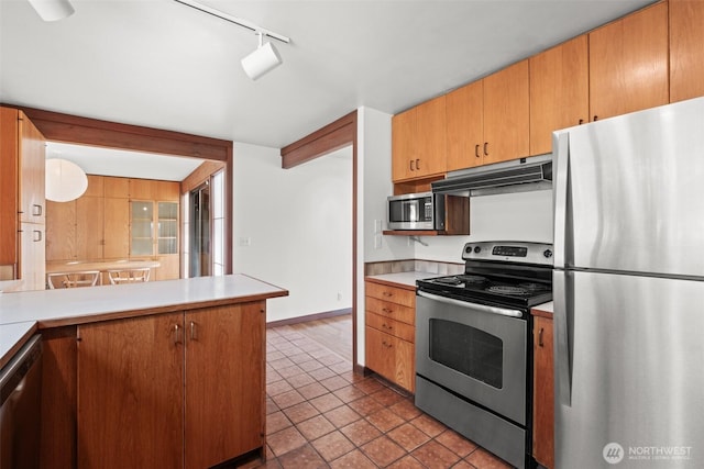kitchen featuring tile patterned flooring, light countertops, under cabinet range hood, a peninsula, and appliances with stainless steel finishes