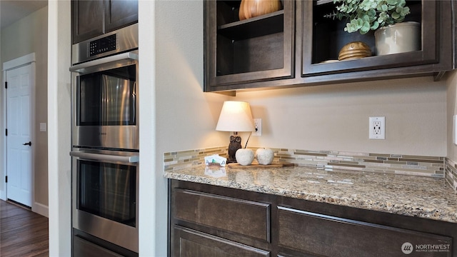 kitchen with double oven, tasteful backsplash, light stone countertops, and dark brown cabinets