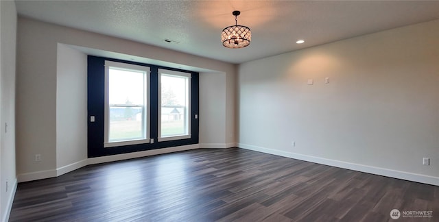 empty room with a notable chandelier, dark wood-type flooring, baseboards, and a textured ceiling