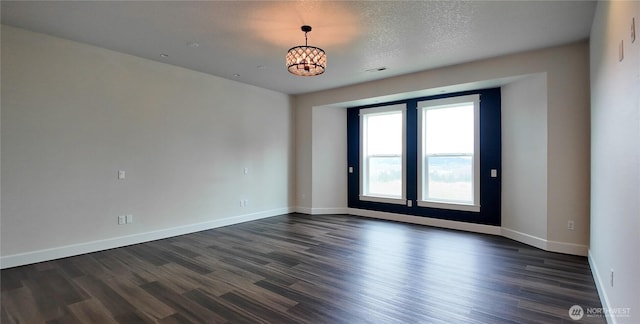 spare room with a notable chandelier, a textured ceiling, baseboards, and dark wood finished floors