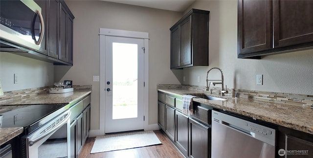 kitchen featuring stainless steel appliances, a sink, light wood-style flooring, light stone countertops, and dark brown cabinetry