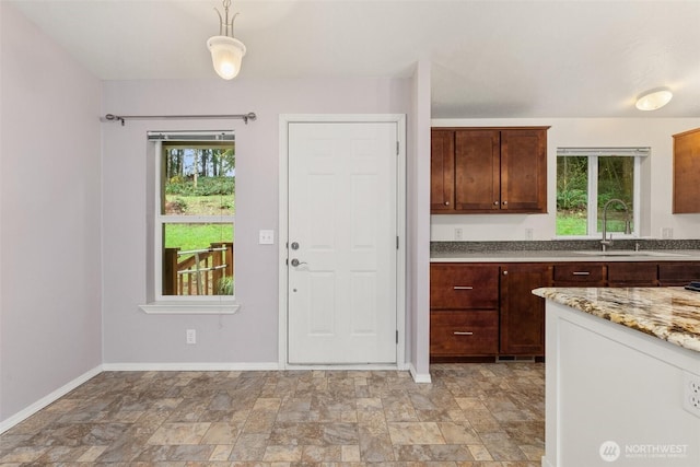 kitchen featuring a sink, stone finish flooring, baseboards, and light stone counters
